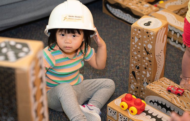Toddler in a toy hard hat playing with wooden blocks