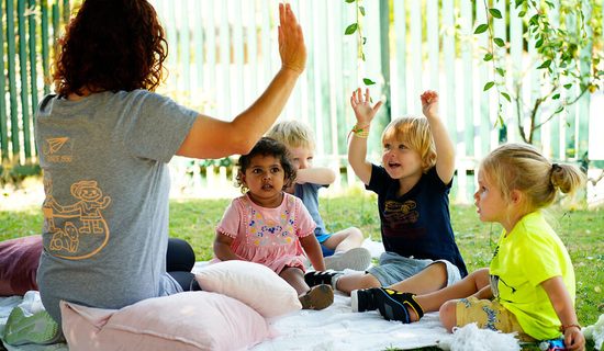 Educator and toddlers waving their hands in the air in the garden