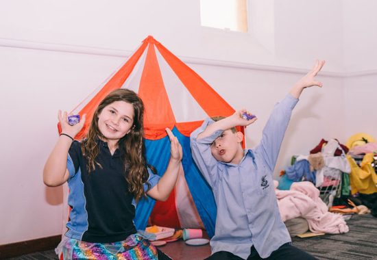 Two school-age children cheering in front of a play tent