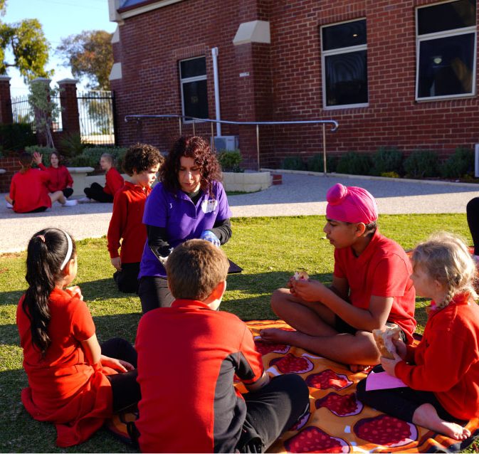 School-age children on picnic rugs on the lawn beside a brick building